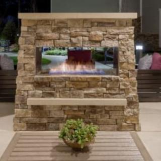 A cozy outdoor stone fireplace on a patio, surrounded by comfortable seating and a potted plant.