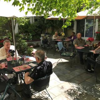 A group of people enjoying their meals at an outdoor restaurant patio under sun umbrellas.