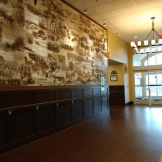 A spacious restaurant lobby featuring a decorative wall mural and wooden flooring, illuminated by natural light.