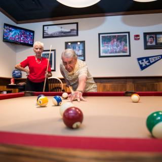 Two seniors enjoying a game of billiards in a cozy game room.
