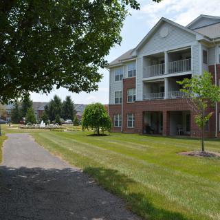 A sunny day view of a residential apartment building with a paved pathway and well-kept grass.