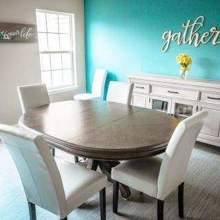 A modern dining room with a wooden table and white chairs, featuring a bright turquoise accent wall.