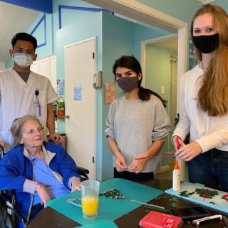 A group of caregivers and an elderly individual interact in a healthcare setting.