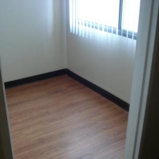 A small, empty room with a wooden floor and natural light coming through a window.