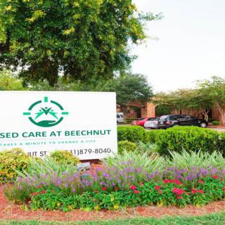 The image shows the entrance sign for a nursing home surrounded by trees and flowers.