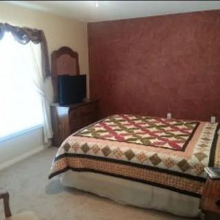 A cozy bedroom with a quilt-covered bed, dresser, and television.