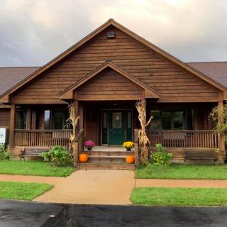 A cozy wooden house with autumn decorations on the porch, including pumpkins and flowers.