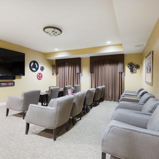 A cozy home theater setup with multiple rows of comfortable gray chairs facing a large television.