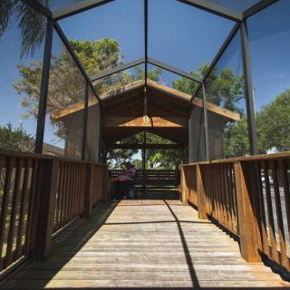 A wooden gazebo with a pathway leading towards it, surrounded by trees on a sunny day.
