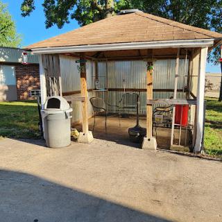 A wooden shelter with open sides, featuring a garbage can and some storage space in a sunny outdoor area.