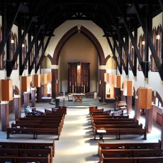 A serene view of a church interior featuring wooden beams and rows of pews.