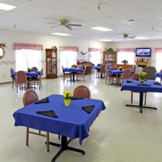 A spacious dining area with tables covered in blue tablecloths, set in a well-lit community space.