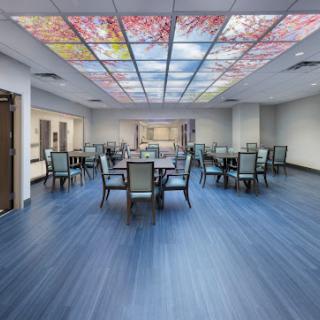 A spacious and well-lit dining area featuring a colorful stained glass ceiling, surrounded by tables and chairs.