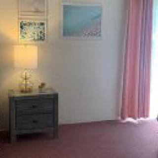 A minimalist bedroom with soft pink curtains, a side table with a lamp, and wall art.