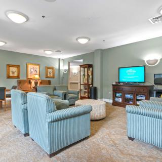 A cozy living room with armchairs, a television, and decorative paintings.