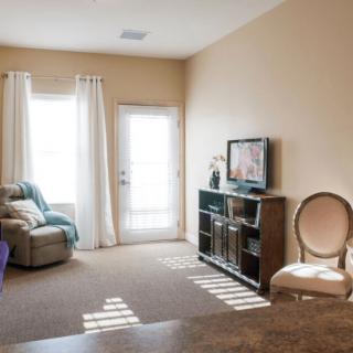A cozy living room with a sofa, TV, and large windows letting in natural light.