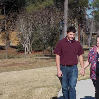 A couple walking hand in hand along a park pathway on a sunny day.