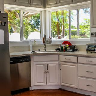 A bright, modern kitchen with white cabinets and large windows.