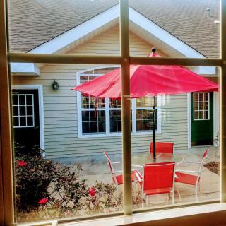 View through a window overlooking a patio with red chairs and umbrella.