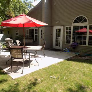 A cozy backyard patio featuring a red umbrella, outdoor table, and chairs on a sunny day.