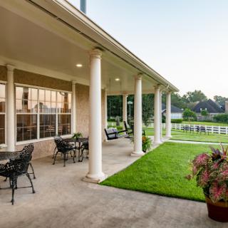 A serene outdoor patio area with columns, chairs, and a well-maintained lawn.