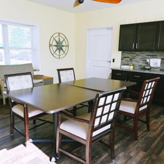 A cozy dining room with a dark wooden table and chairs, featuring a small kitchen area in the background.