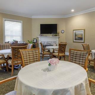 A cozy dining area with several round tables and wicker chairs, featuring a television and decorative elements.