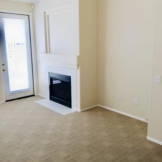 A cozy empty room featuring a fireplace, carpeted floor, and a door leading outside.