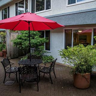 A cozy patio setup with a red umbrella over a table and chairs, surrounded by potted plants.