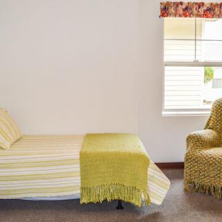 A minimalist bedroom with a single bed, yellow-themed bedding, and an armchair by the window.