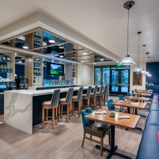 A modern restaurant interior featuring a sleek bar and a stylish dining area with wooden tables and chairs.
