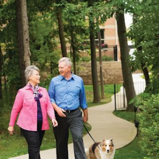A happy couple enjoys a leisurely stroll in the park with their dog.