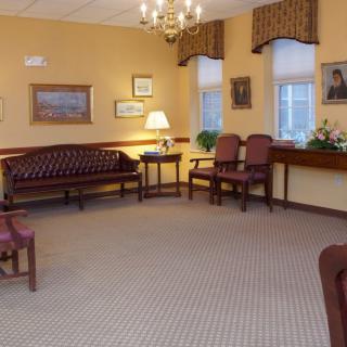 A cozy waiting room with traditional furniture, including chairs, couches, and a table, adorned with paintings and a lamp.