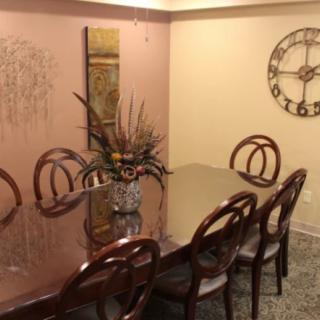 A well-decorated dining room featuring a glass table with six chairs, wall art, and a large decorative clock.