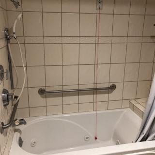 A bathroom featuring a bathtub with a showerhead and grab bar against tiled walls.