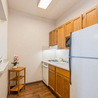 A compact kitchen with wooden cabinets, equipped with a refrigerator, stove, and dishwasher.