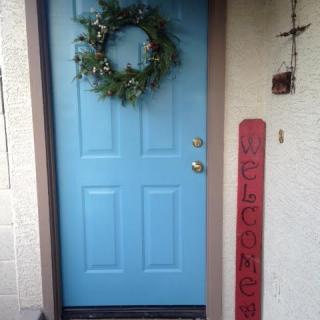 A blue front door adorned with a wreath and a red welcome sign.