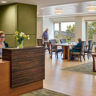 A well-lit reception area with a desk, several tables, and chairs, featuring natural light and a vase of flowers.
