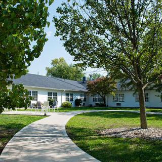 A charming residential house with a pathway leading through a well-maintained yard surrounded by trees.

