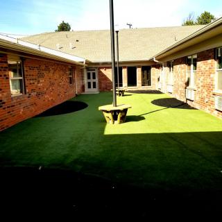 A sunny courtyard with artificial grass surrounded by brick buildings.