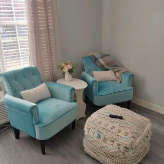 A cozy living room corner with blue chairs and a patterned ottoman.