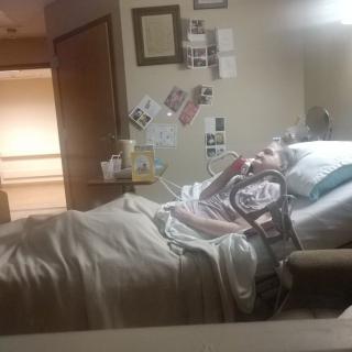 A patient resting in a hospital bed surrounded by medical equipment and personal items.