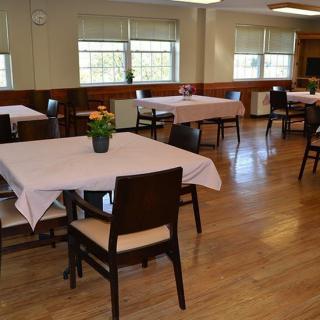 A spacious dining room with neatly arranged tables and chairs, adorned with tablecloths and potted plants.