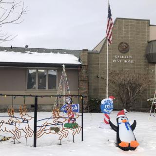 A snowy scene outside a town hall, featuring festive decorations including a penguin and candy canes, with an American flag waving nearby.