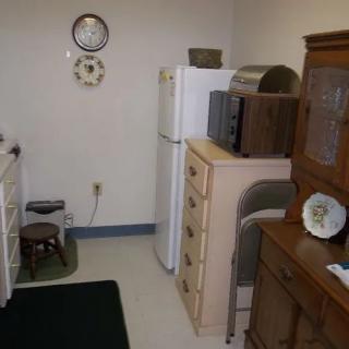 A small kitchen area with a fridge, microwave, and various wooden furniture pieces.