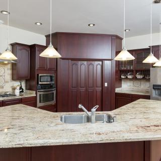 A modern kitchen with granite countertops, wood cabinets, and pendant lighting.