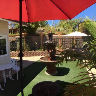 A sunlit patio with a red umbrella, decorative fountain, and outdoor seating.