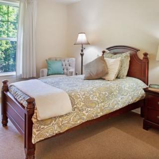 A cozy bedroom with a wooden bed frame and decorative pillows, illuminated by a nearby lamp next to a window.