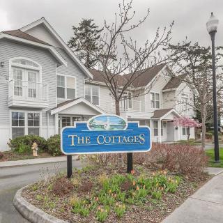 A residential area featuring a sign for 'The Cottages' with manicured landscaping and overcast skies.