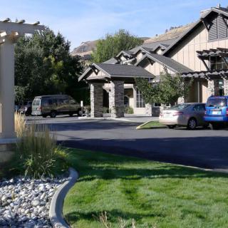 A suburban house with a driveway and parked cars, surrounded by landscaped greenery.